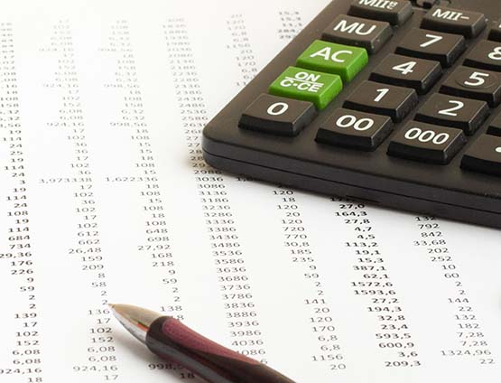 calculator and pen on a financial spreadsheet statement with columns of numbers
