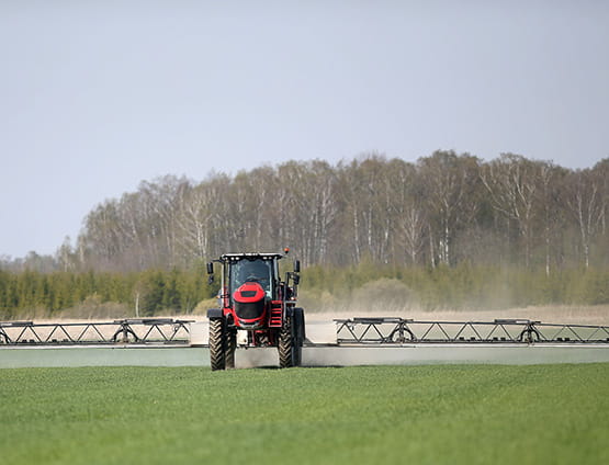 Tractor with high wheels spraying fertilizer on crops