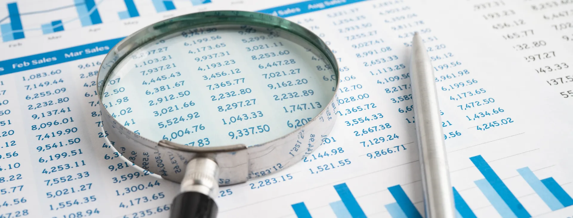 Close up view of magnifying glass over financial spreadsheet and bar charts for detailed business data inspection with analysis