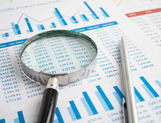 Close up view of magnifying glass over financial spreadsheet and bar charts for detailed business data inspection with analysis