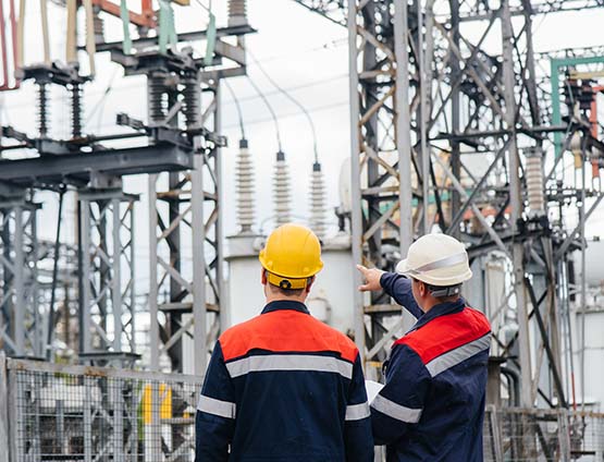 Two men inspect high-voltage equipment at power plant.